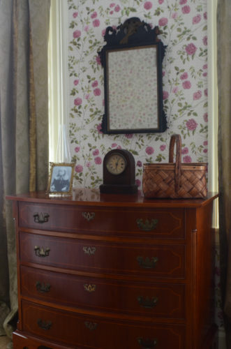 The bureau in Emily Dickinson's bedroom with a clock, a basket, and a photograph of her nephew Gib on it.