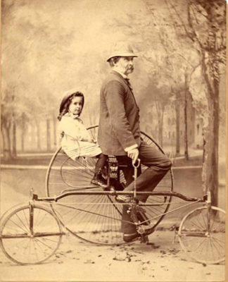 black and white photograph of Higginson with his young daughter upon a two-person bicycle