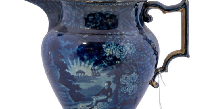 Blue Staffordshire ceramic transferware pitcher with blue glaze showing a scene of a man sitting across from a monument with the name "Franklin" at the base with a tall ship in the distance, known as "Lafayette at Franklin's tomb".