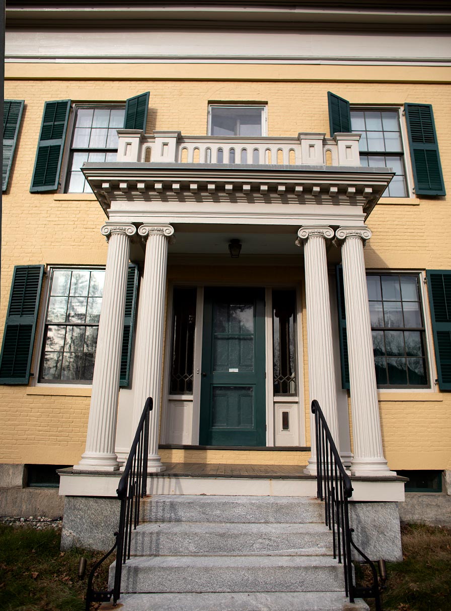 An imposing view up the front steps of the yellow brick Homestead. Fluted double columns flank the the green front door.