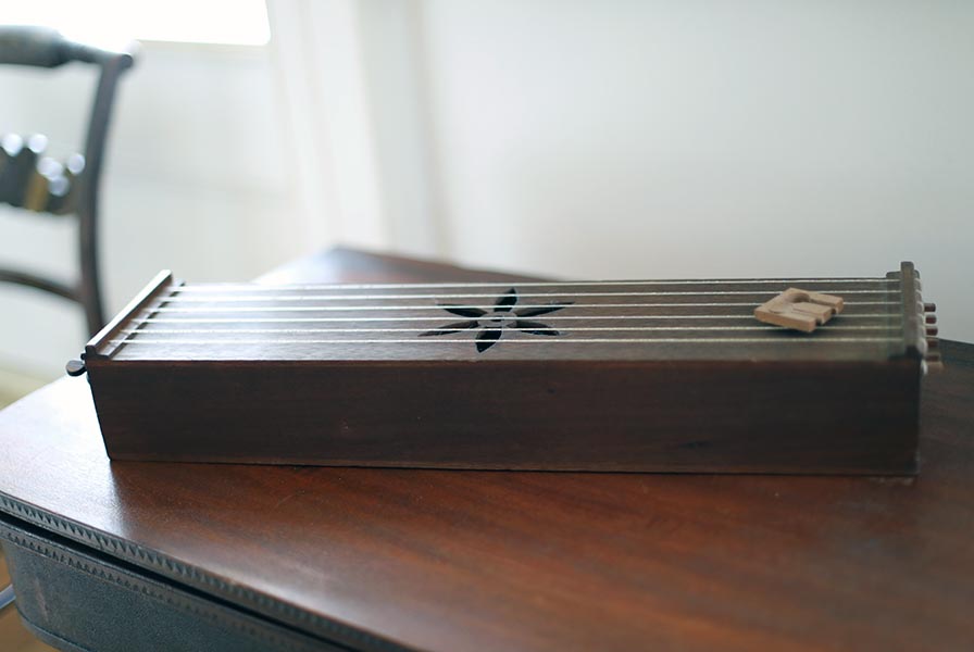 The harp is a wooden rectangular box fretted with strings. Cut outs in the top helped the air move through.