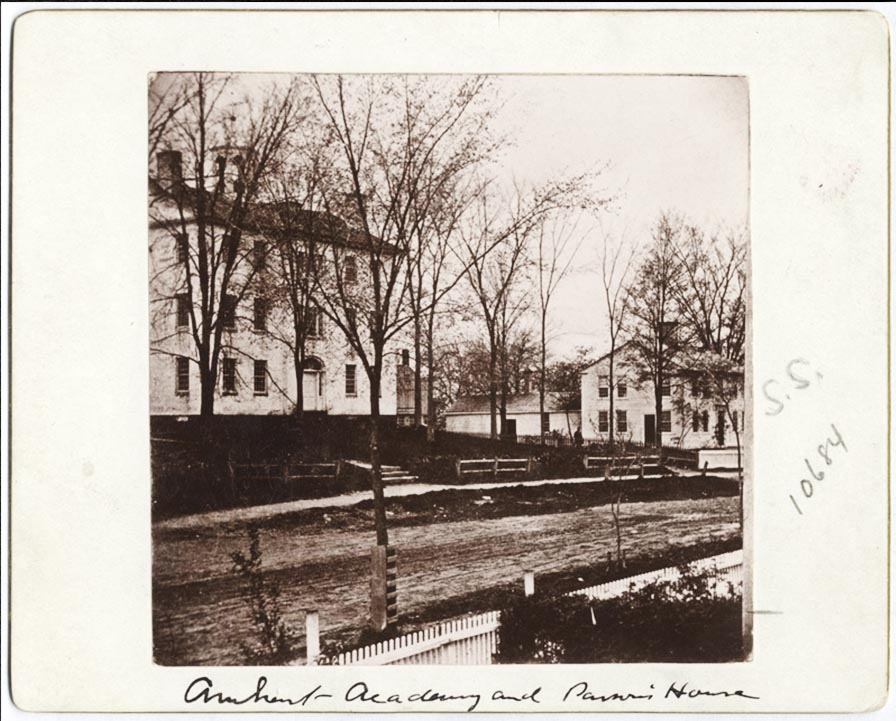 Street scene with a three-story building to the left. The building is square and symmetrical, with tall, paned windows.