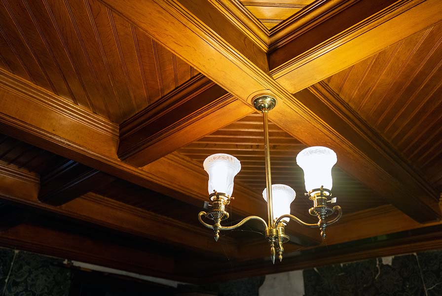 Coffered ceiling of polished warm wood illuminated by a chandelier.