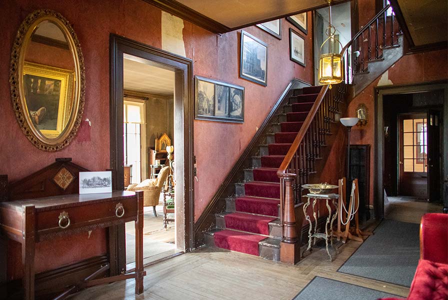 Glimpse of The Evergreens parlor from an entrance hall with deep red, dark wood, and gilt finishings.