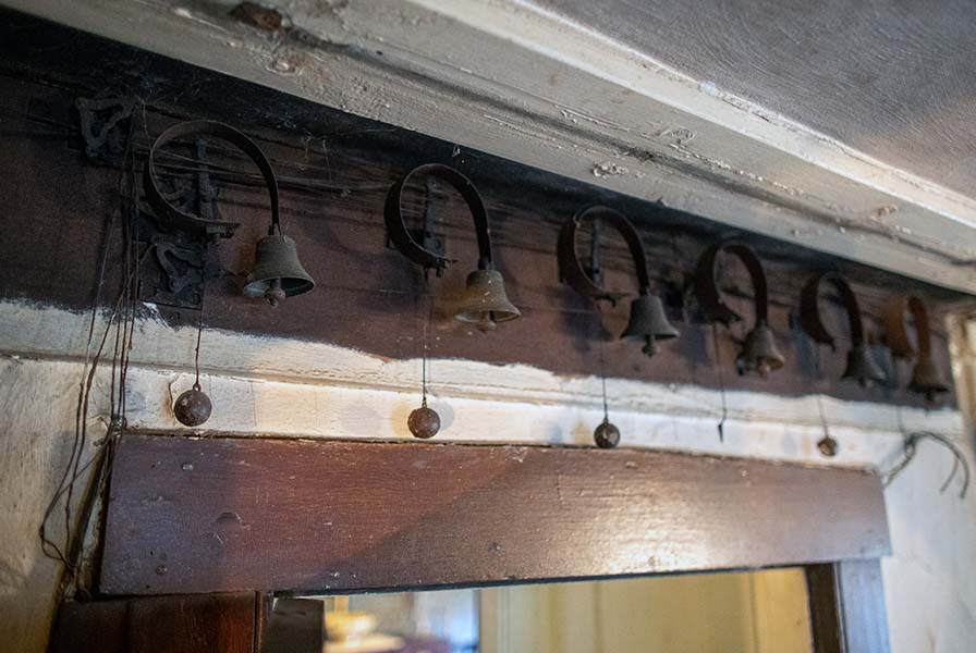 Seven iron call bells affixed above a door frame. Ball-shaped weights are suspended from the bells with wires.