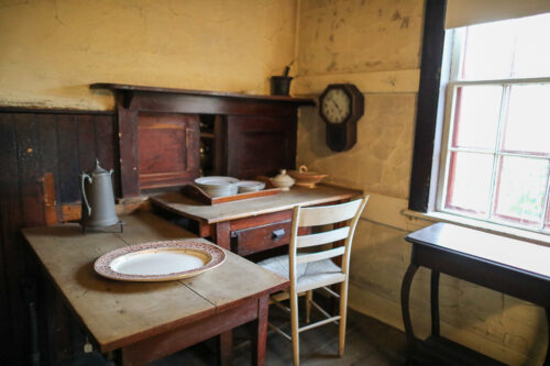 photograph of the kitchen in the Evergreens. There are plates, teapots, and preparation area. A small sliding door opens to the dining room.