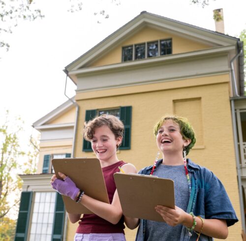 two students hold clipboards outside the Homestead