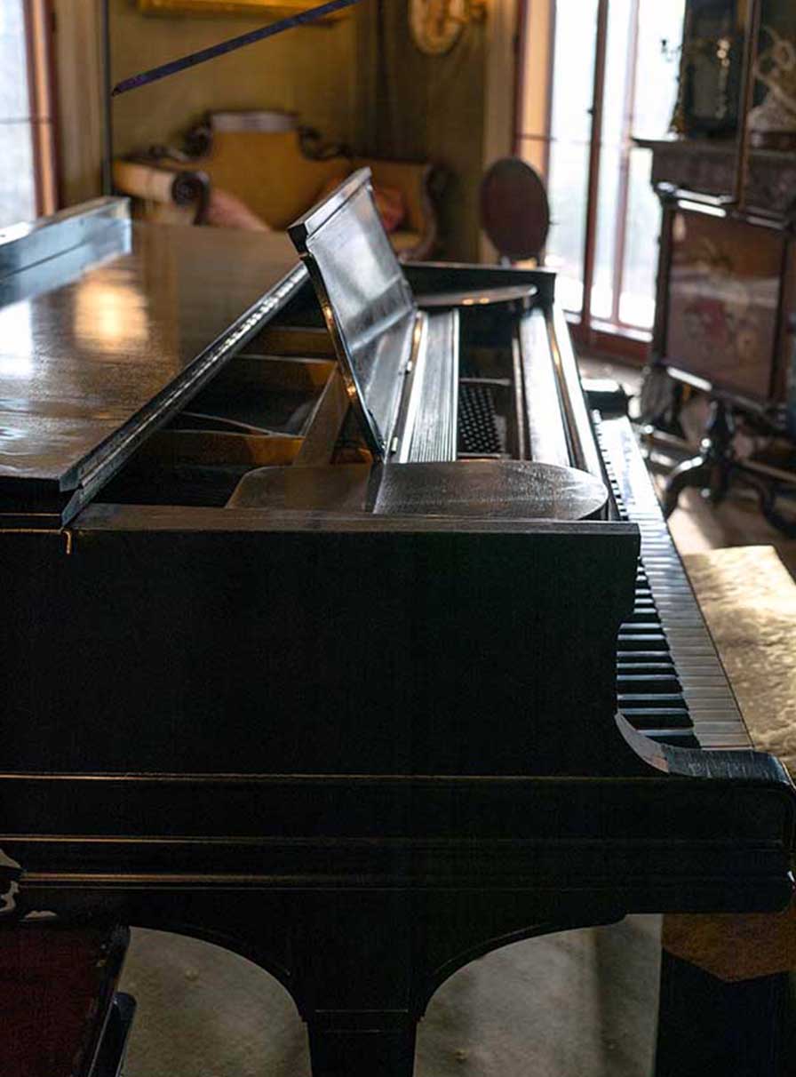 Side view of a black grand piano with a gold brocade seat covering.