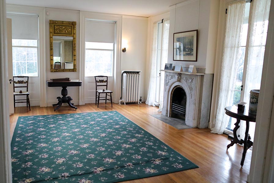 Two windows look south, a heavy, gilded mirror between; two french doors flank the marble hearth at right.