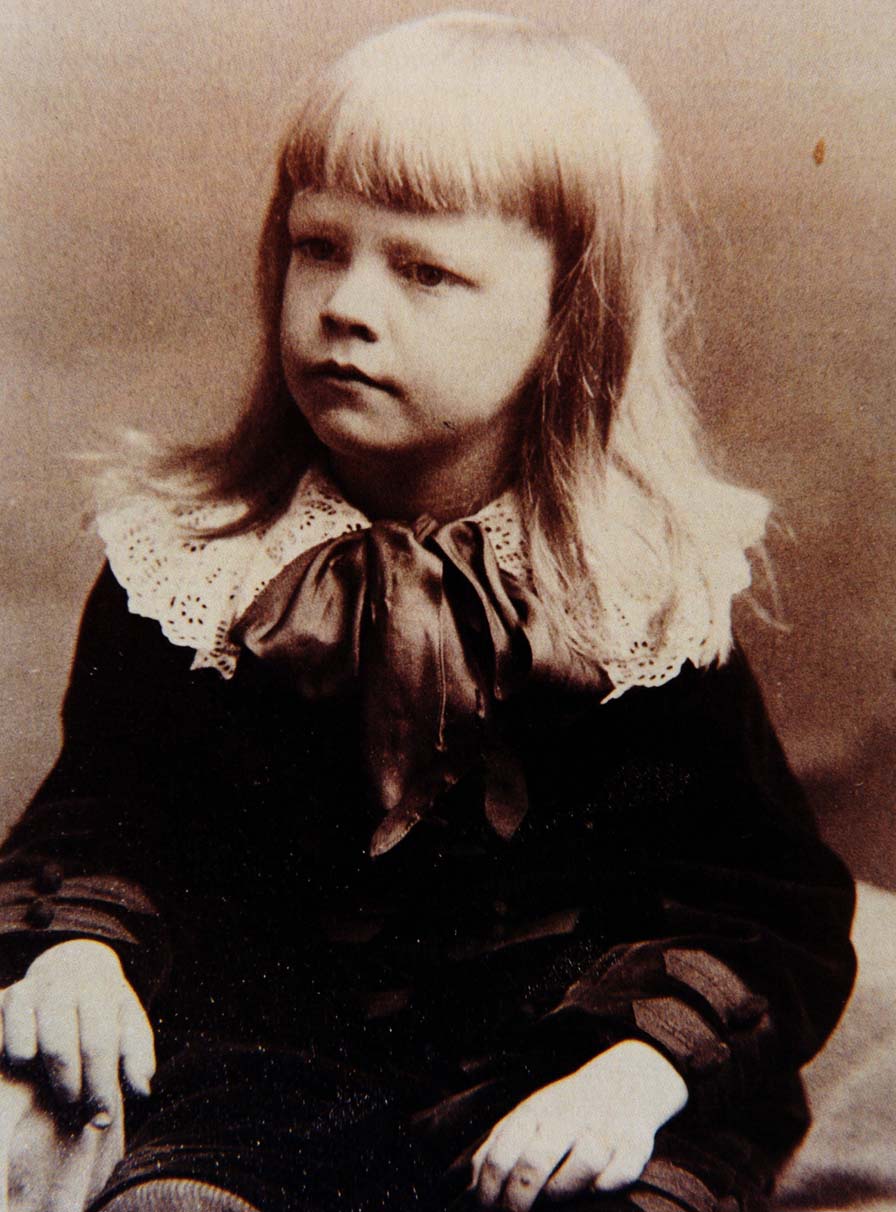 A seated young boy with long, fair hair. He wears a velvet suit with lace ruff and a ribbon at his throat