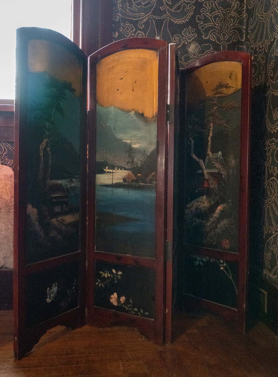 Folded wood screen with painted panels depicting a rural Japanese scene of buildings surrounding a mountain lake.