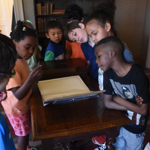 Photograph of children gathering around a book in the Dickinson library