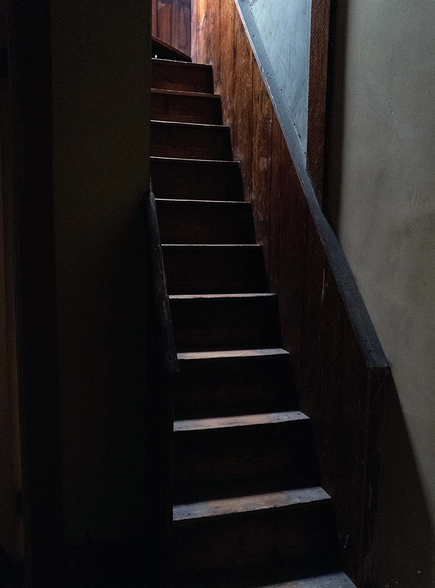 A steep, narrow wooden staircase in heavy shadows.