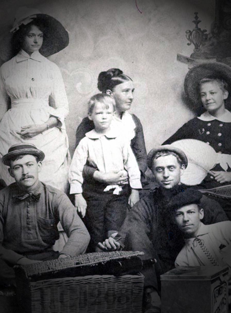 Historic photograph of a seated woman holding a fair-haired young boy on her lap. He wears a white shirt with rounded collar.