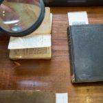 Closeup of a hand holding a magnifying glass over antique books.