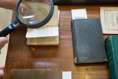 Closeup of a hand holding a magnifying glass over antique books.