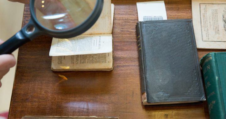 Closeup of a hand holding a magnifying glass over antique books.