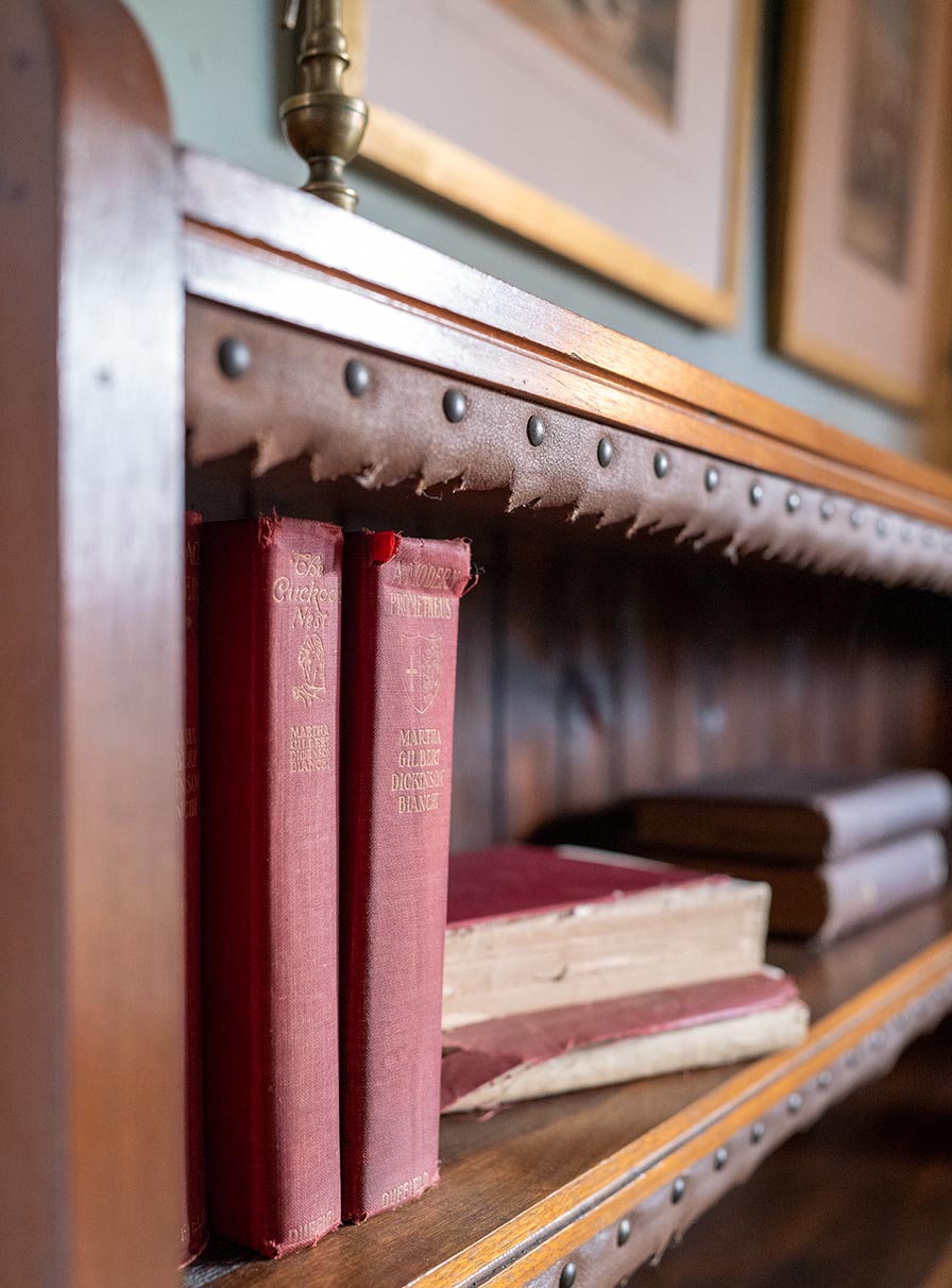 Six red, cloth-bound books rest on the top shelf of a wooden bookshelf