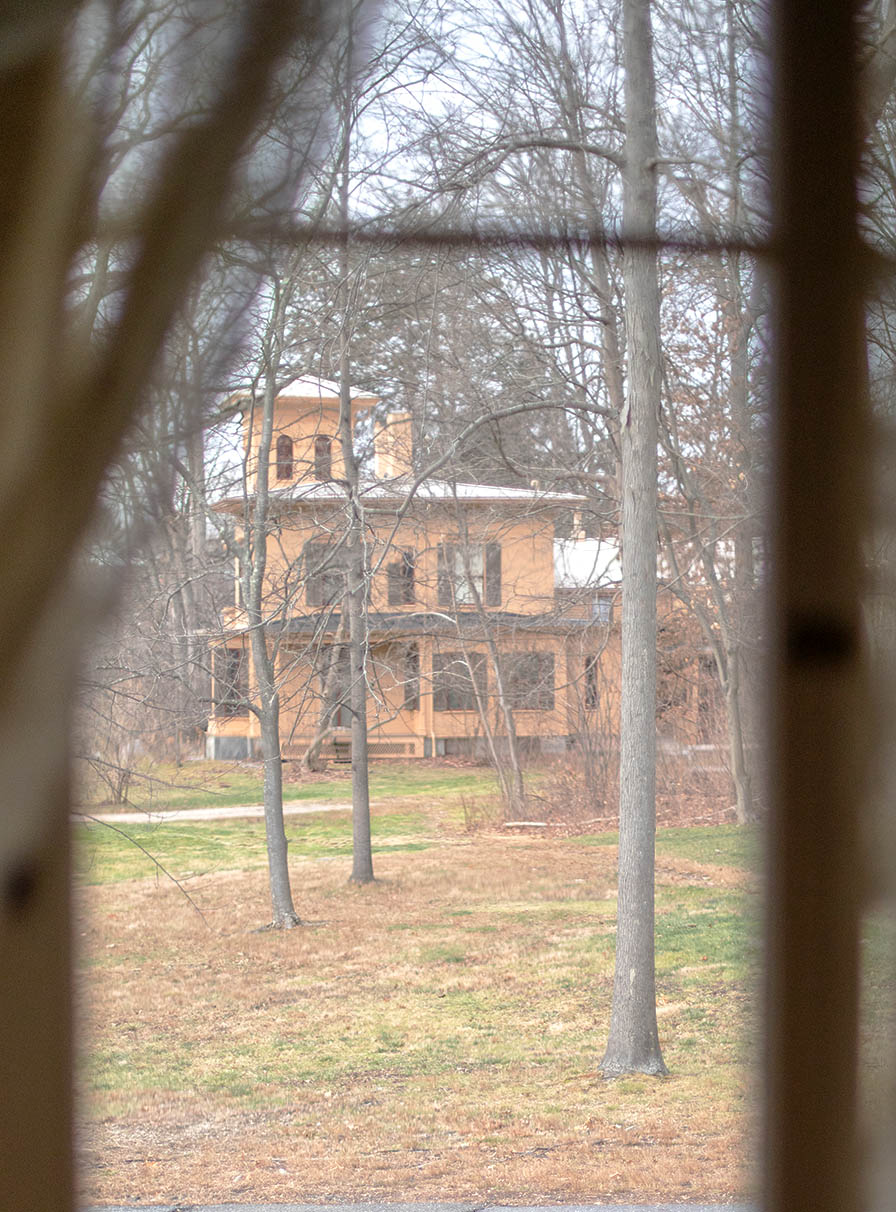 A yellow, Italianate house seen through a paned window with sheer curtains.