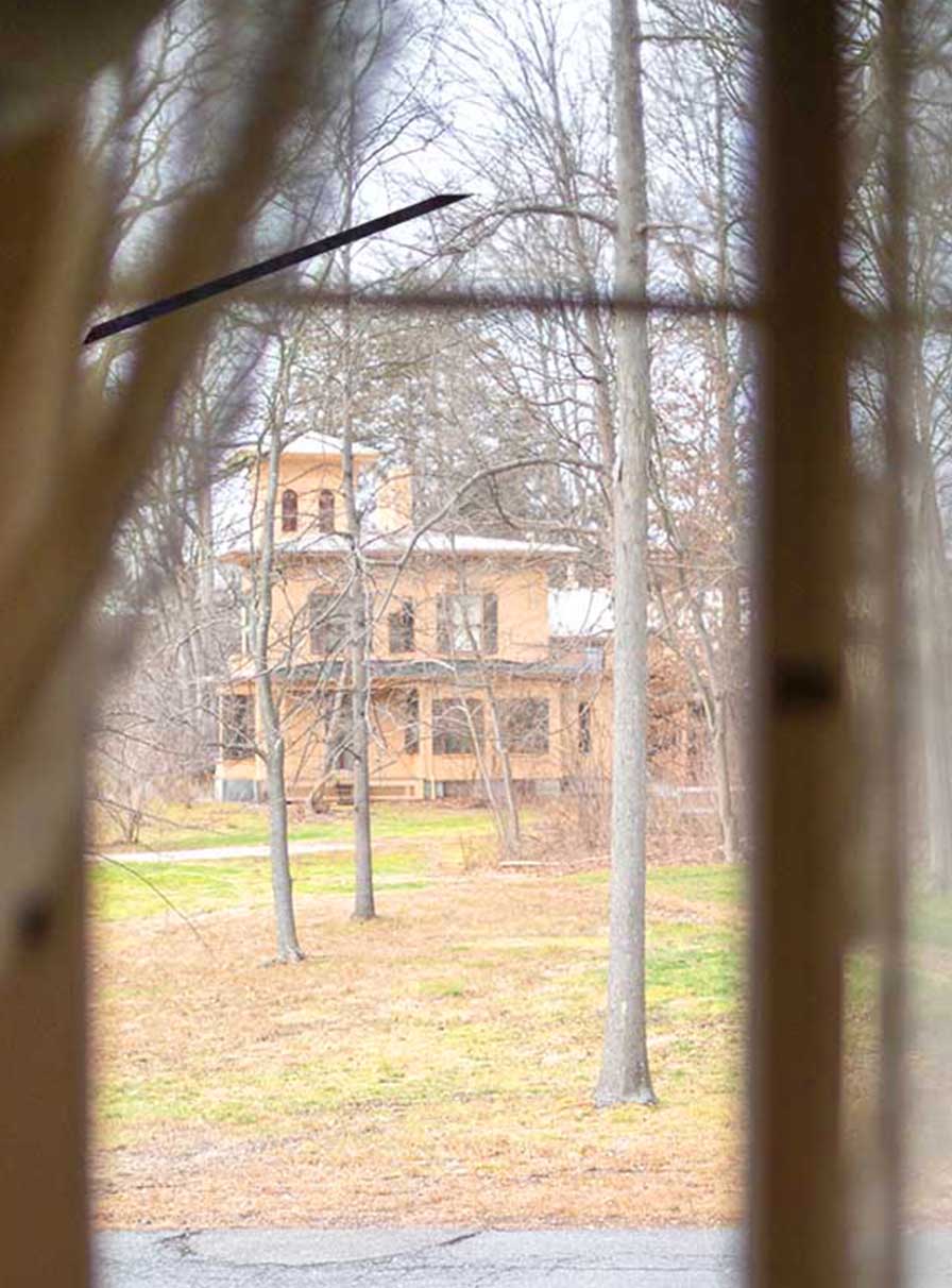 A yellow, Italianate house seen through a paned window with sheer curtains.