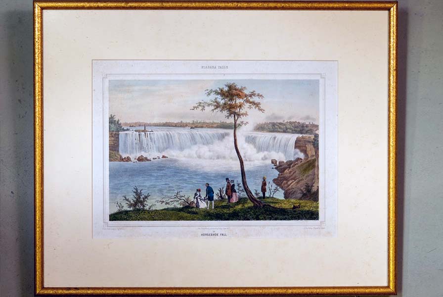 Print labeled "The Falls of Niagara." Two large waterfalls with plumes of mist. Minuscule people gather near one of the falls