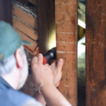 a man uses a flashlight to investigate the beams under the homestead roof