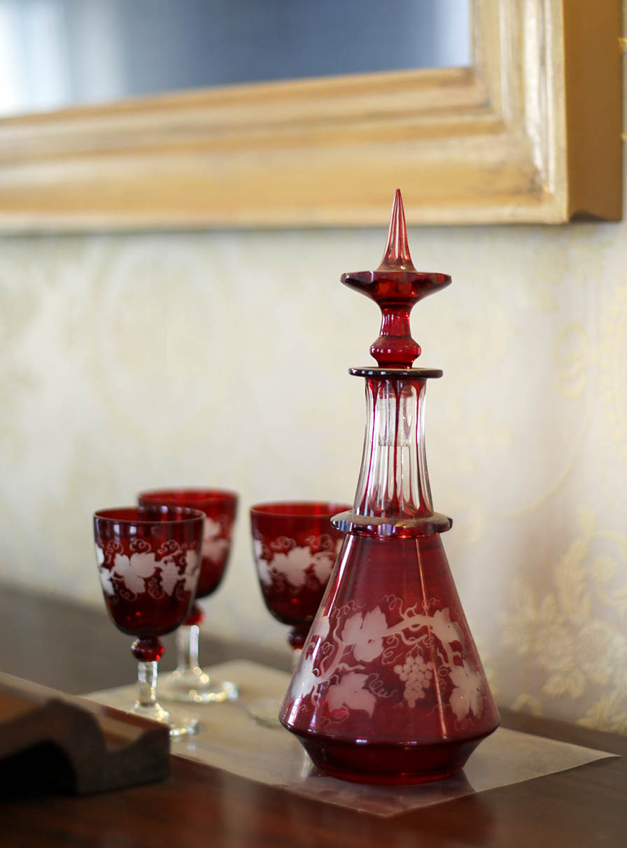 Matching bohemian cut glass decanter and cordial glasses sit atop the piano.