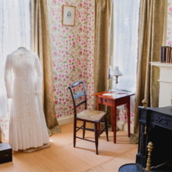 Image of Dickinson's room featuring her writing desk and white dress