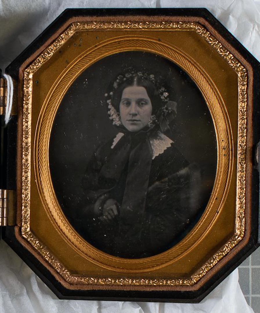 Young woman wearing a lace collar and floral-trimmed bonnet tied with a wide ribbon