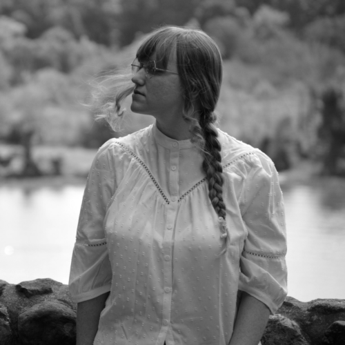 a woman wearing glasses and a white dress looks off into the distance