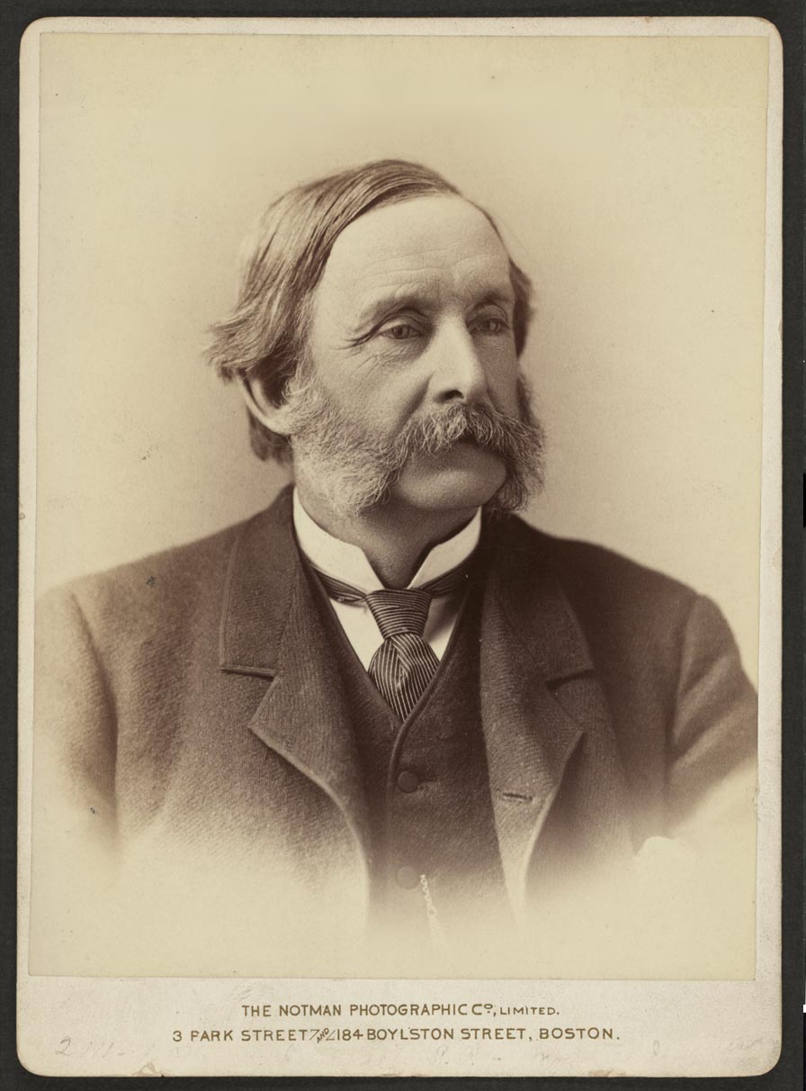 Sepia photograph of mature man with graying mustache and mutton chops wearing a suit, waistcoat, and striped tie.