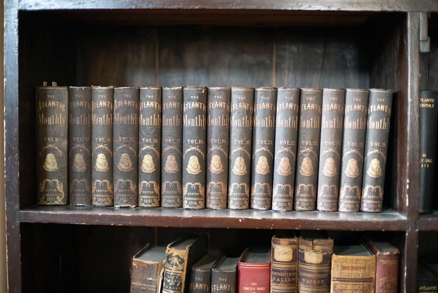 A row of bound Atlantic Monthly vols., dated to the 1860s & 70s. The spines are stamped with the bust of Gov. John Winthrop.