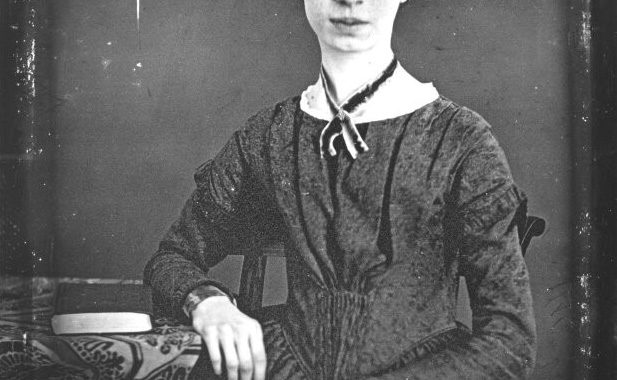 Emily Dickinson daguerreotype, showing the poet seated and facing the viewer, resting one arm on a desk