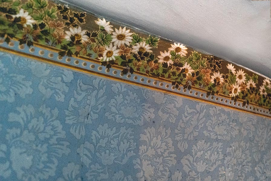 A papered wall in a blue floral pattern. The border features white daisies and greenery with a gold background.