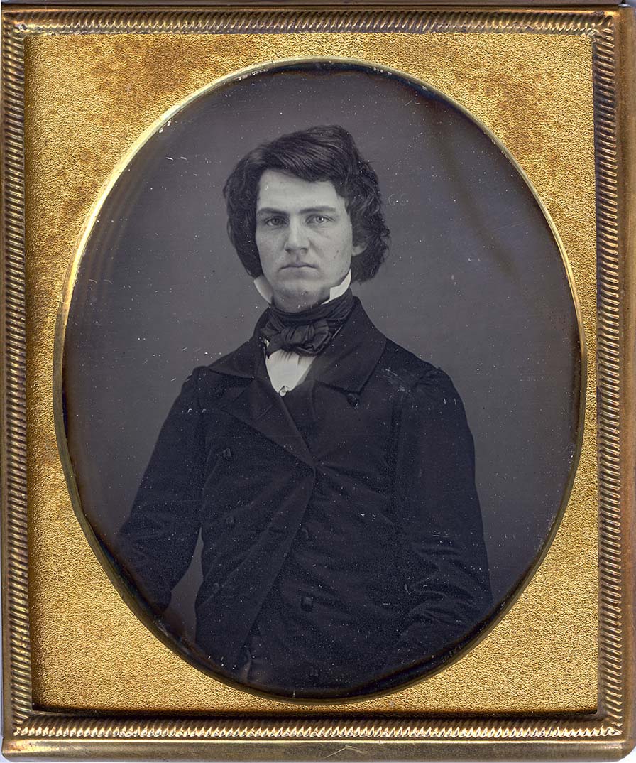 Gilt-framed daguerreotype of a man with a full head of wavy hair. He wears a high collar, cravat and double-breasted jacket.