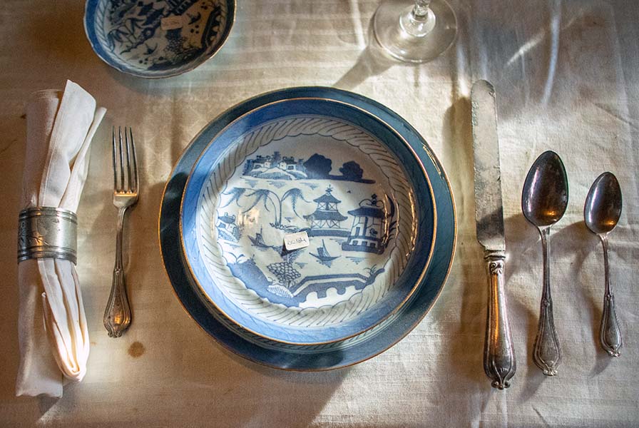 Place setting on a white cloth with silver utensils. The plate and charger are Chinese export porcelain with a blue glaze.