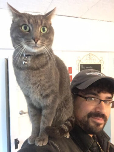 Michael Medeiros appears with a gray cat on his shoulder.