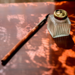 A pen and inkwell sits on Dickinson's writing desk with light cascading through her curtains