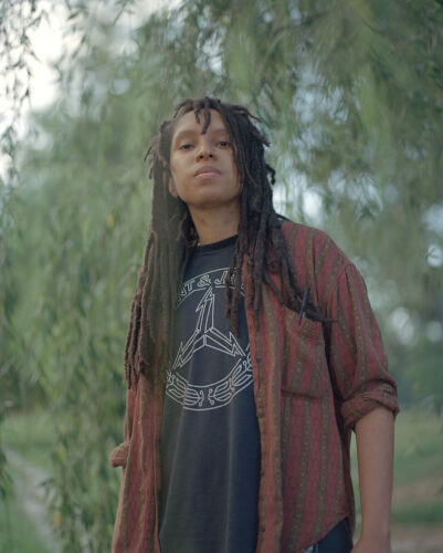 Poet Taylor Johnson looks into the camera in front of a background of foliage