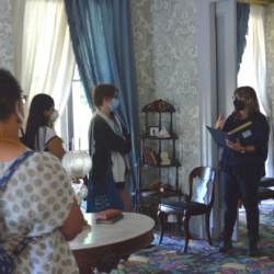 a tour guide is giving a tour of the Homestead parlor. Everyone in the photo is wearing a K95 mask.