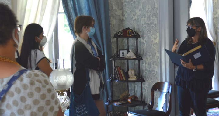 a tour guide is giving a tour of the Homestead parlor. Everyone in the photo is wearing a K95 mask.