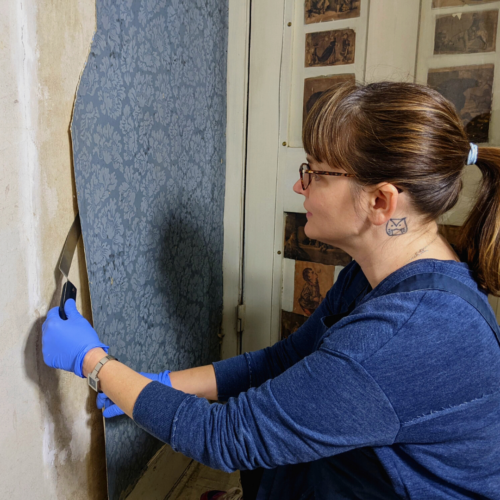 Wallpaper conservationist Carolyn Frisa carefully peels wallpaper from the wall of the Evergreens